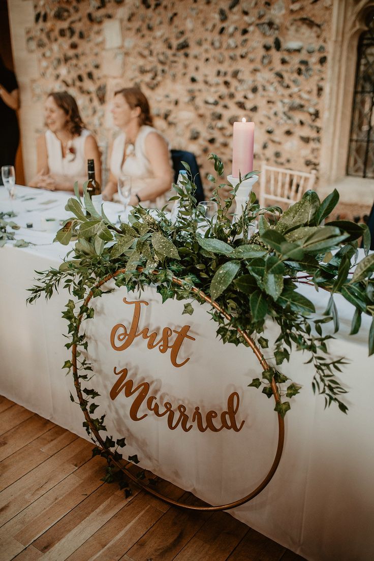 a sign that says just married sitting on top of a table with flowers and greenery