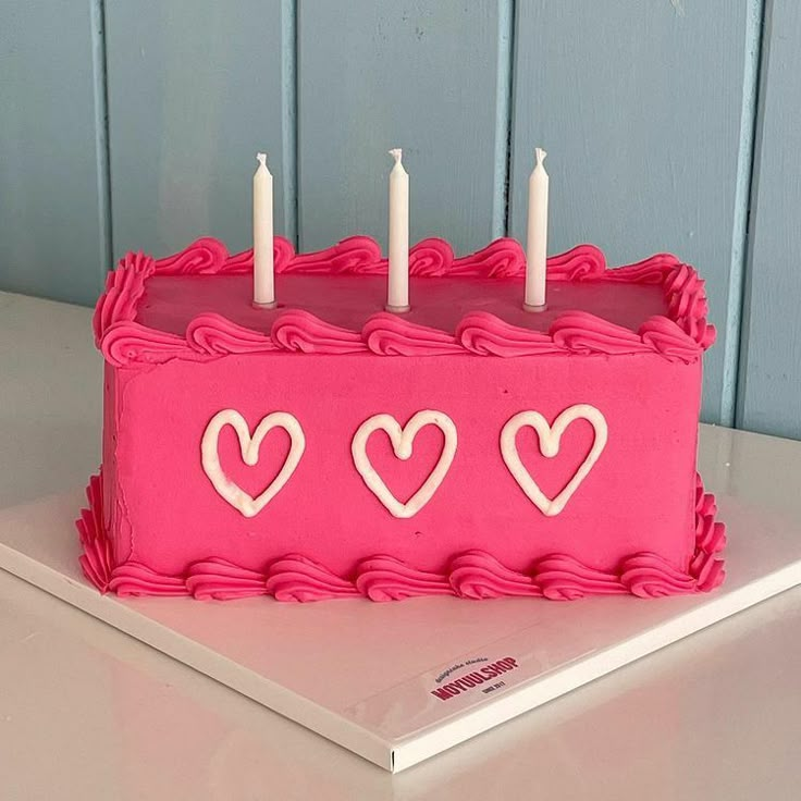 a pink birthday cake with hearts and candles on the top is sitting on a table