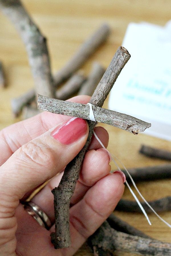 a person is holding a cross made out of sticks and nails on a table next to some twig