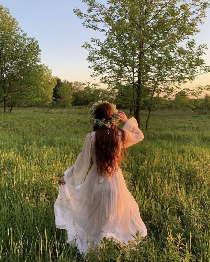 a woman in a white dress is walking through the grass with her back to the camera