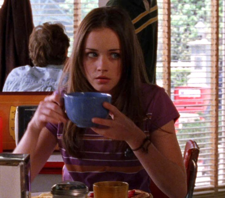 a woman sitting at a table with a bowl in front of her and looking down