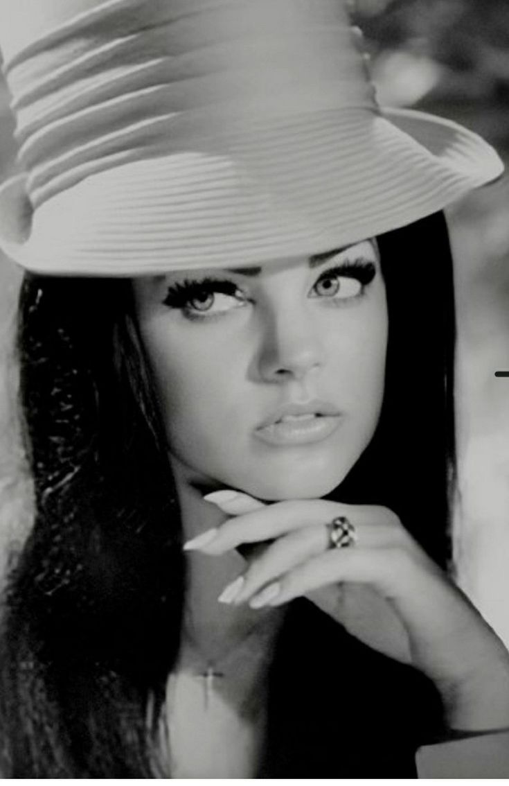 a black and white photo of a woman wearing a hat with her hand on her chin