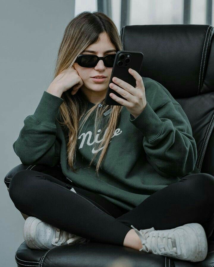 a woman sitting in a chair with her cell phone up to her ear and looking at the screen