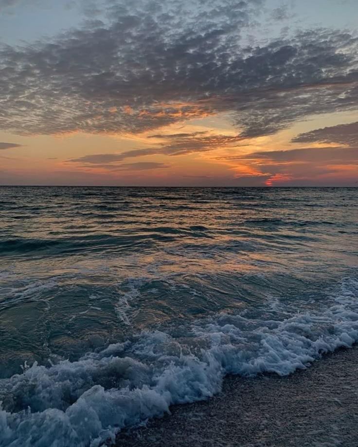 the sun is setting over the ocean with waves crashing on the shore and clouds in the sky