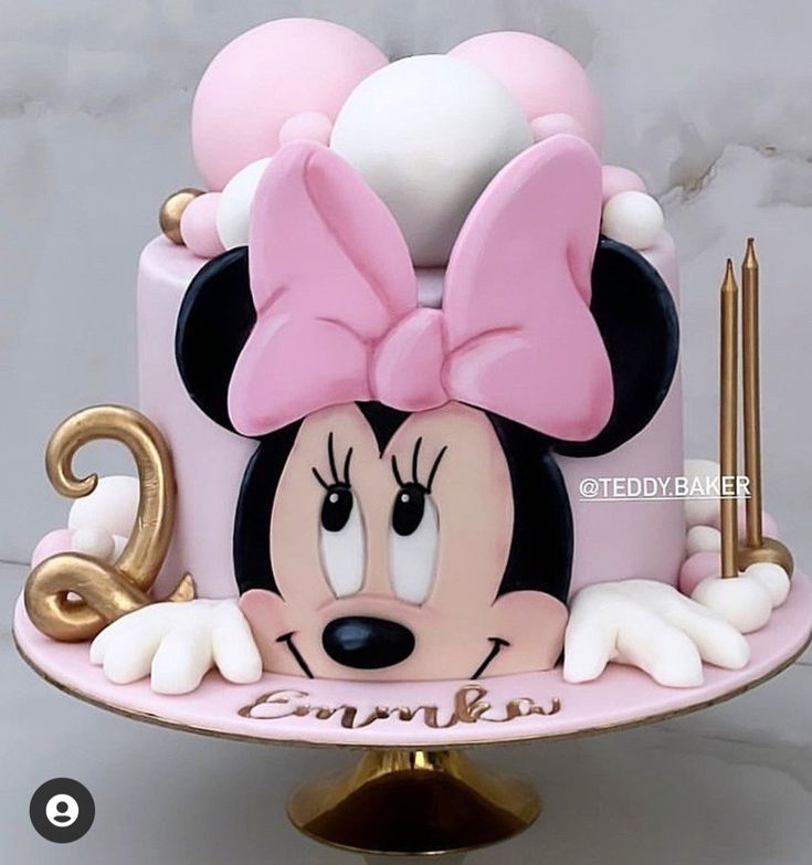 a minnie mouse cake with pink and white icing on a gold plated stand