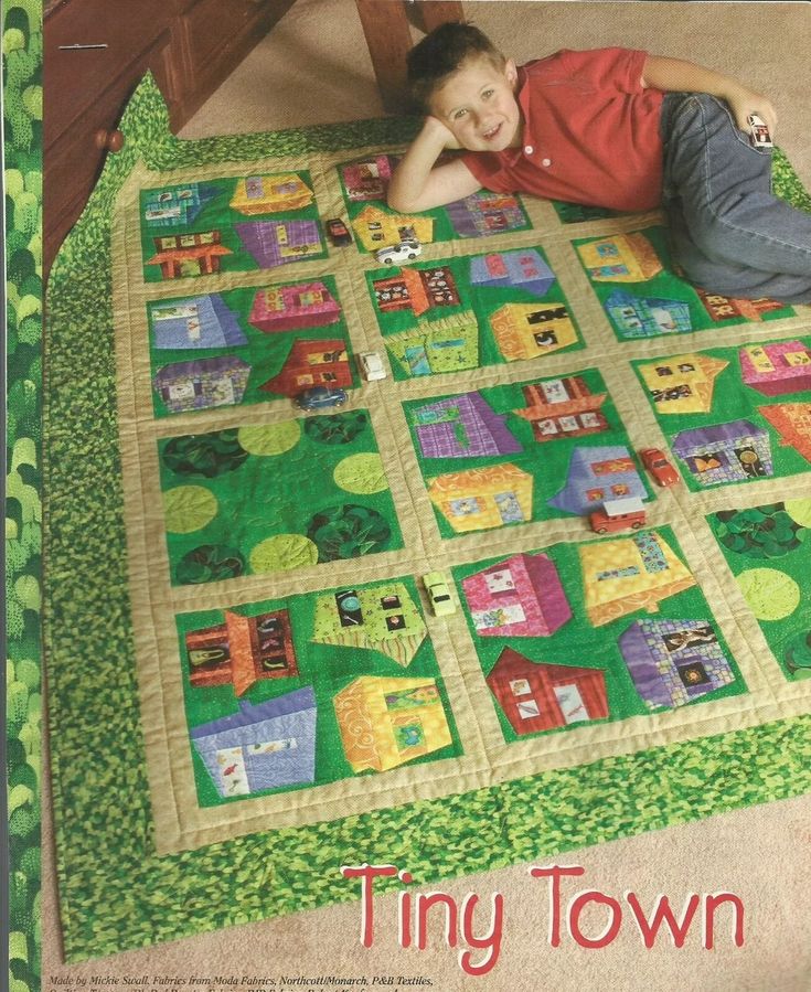 a young boy laying on top of a green and yellow quilted blanket with houses