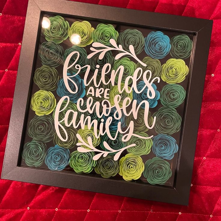 a framed art piece with the words friends are chosen family in it on a red blanket