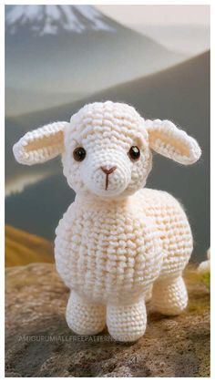 a crocheted white sheep sitting on top of a rock with mountains in the background