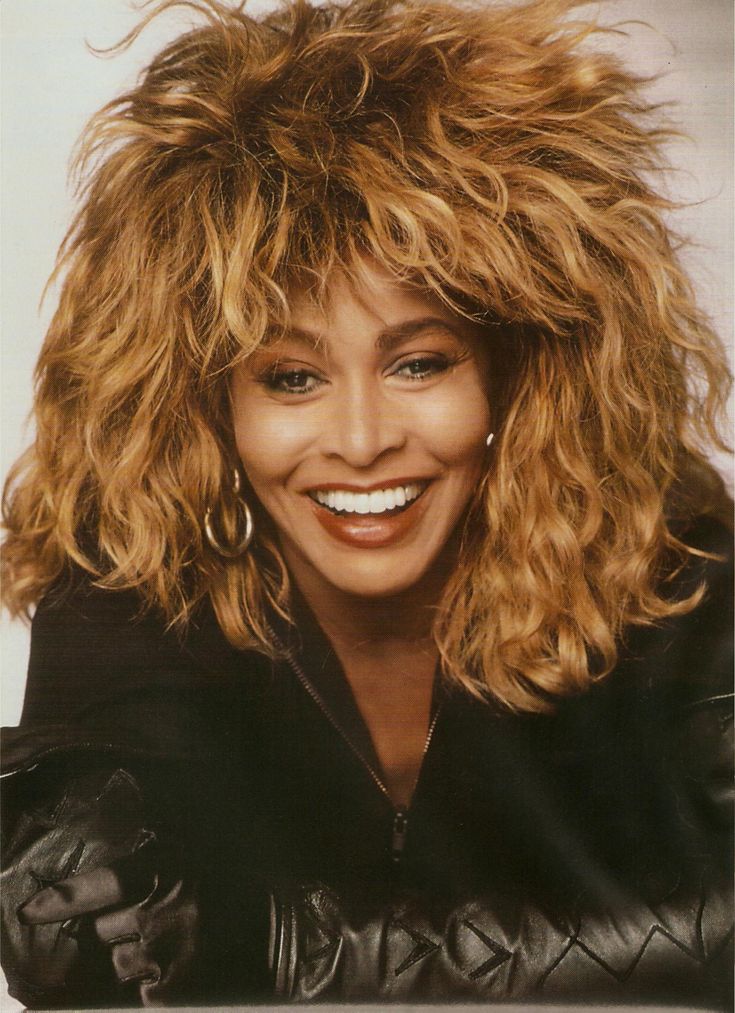 a black and white photo of a woman with curly hair smiling at the camera while wearing a leather jacket