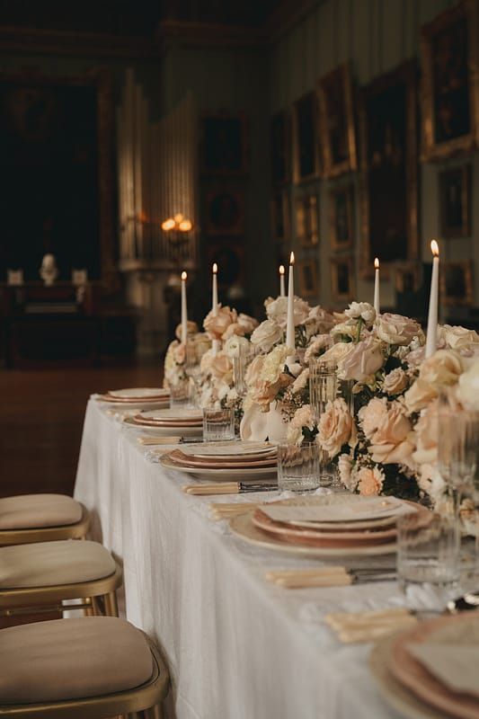 the table is set with white and pink flowers, gold place settings, and candles