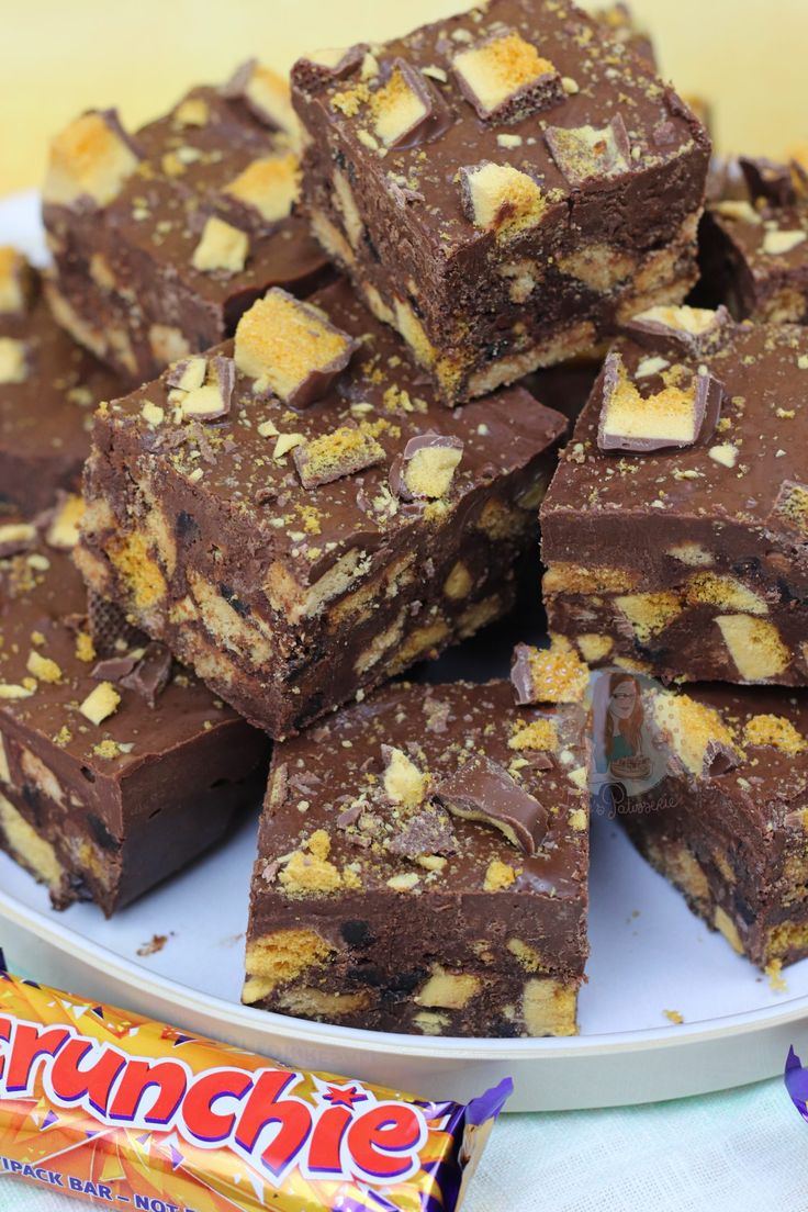 a white plate topped with brownies covered in chocolate and peanut butter pieces next to a candy bar