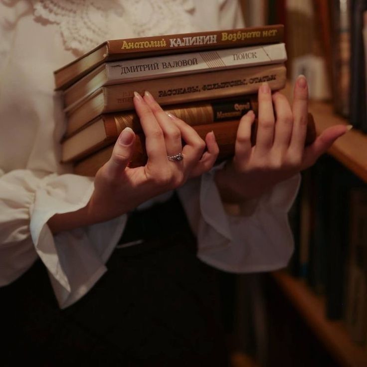 a woman holding several books in her hands while standing next to a book shelf filled with books