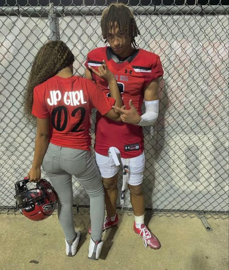 two football players standing next to each other in front of a fence with their hands together