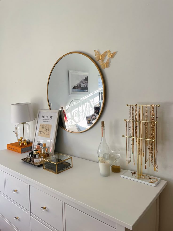 a white dresser topped with a mirror next to a lamp and a vase on top of it