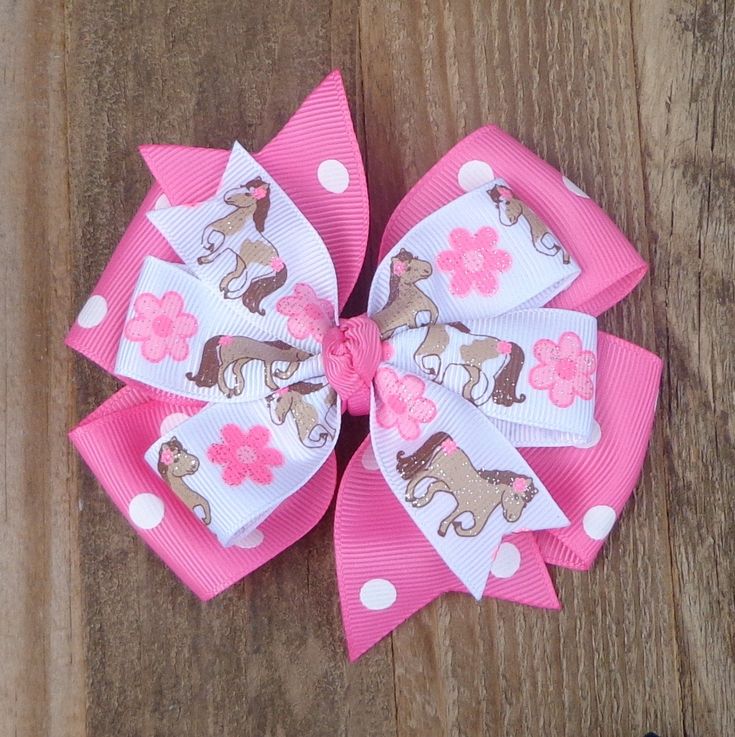 a pink and white hair bow with flowers on it sitting on a wooden surface next to a pair of scissors