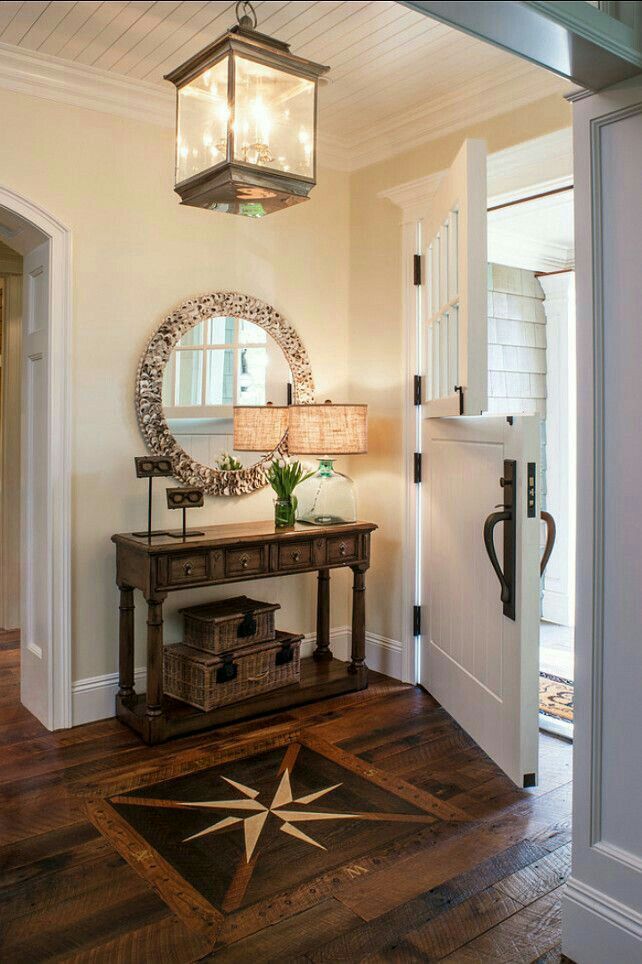 a foyer with a mirror, table and lamp