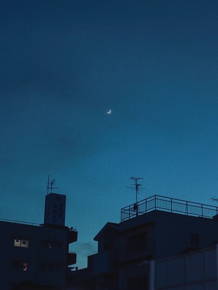 the moon is seen in the sky over some buildings