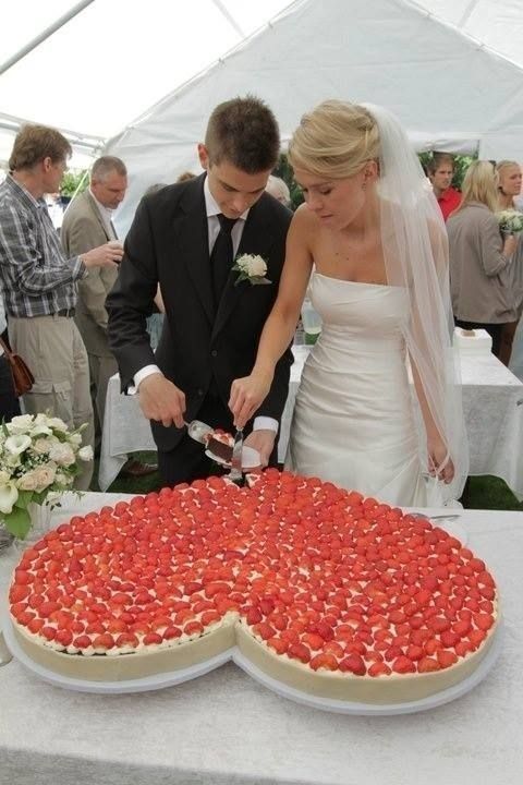 a man and woman cutting into a large pizza on top of a table with people in the background