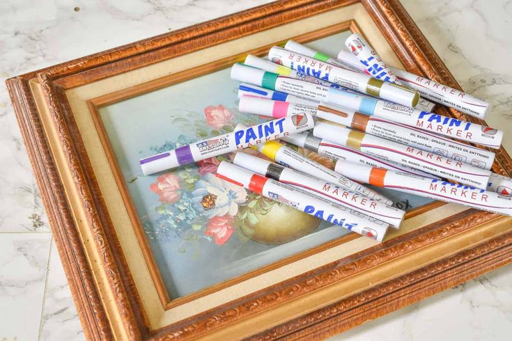 several tubes of paint sitting on top of a painting in a wooden frame next to a vase