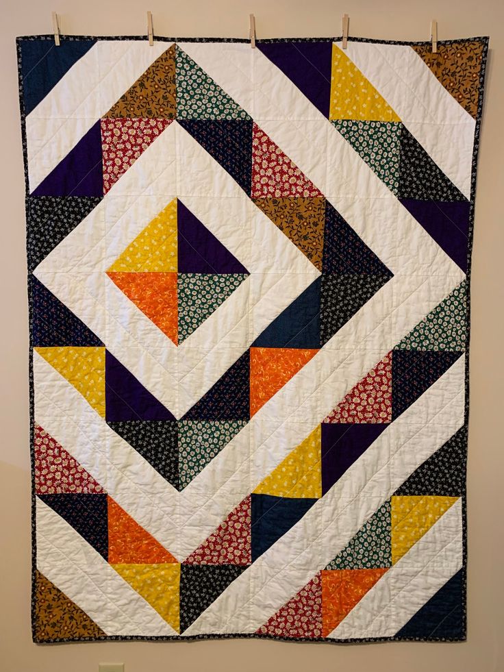 a colorful quilt hanging on a wall in front of a white wall with an orange, yellow and blue design