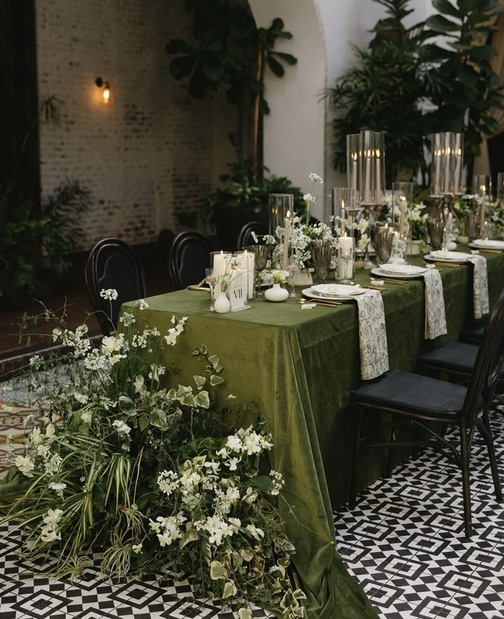 the table is set with green linens and white flowers, candles, and greenery