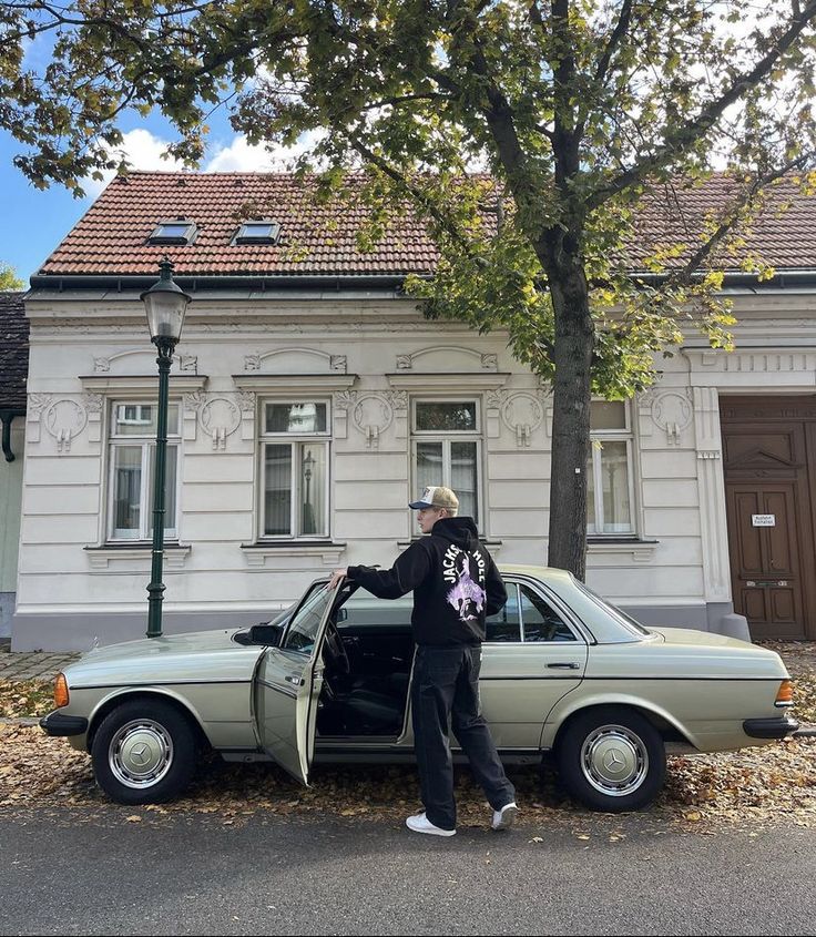 a man standing next to a car with the door open and his hand on the hood