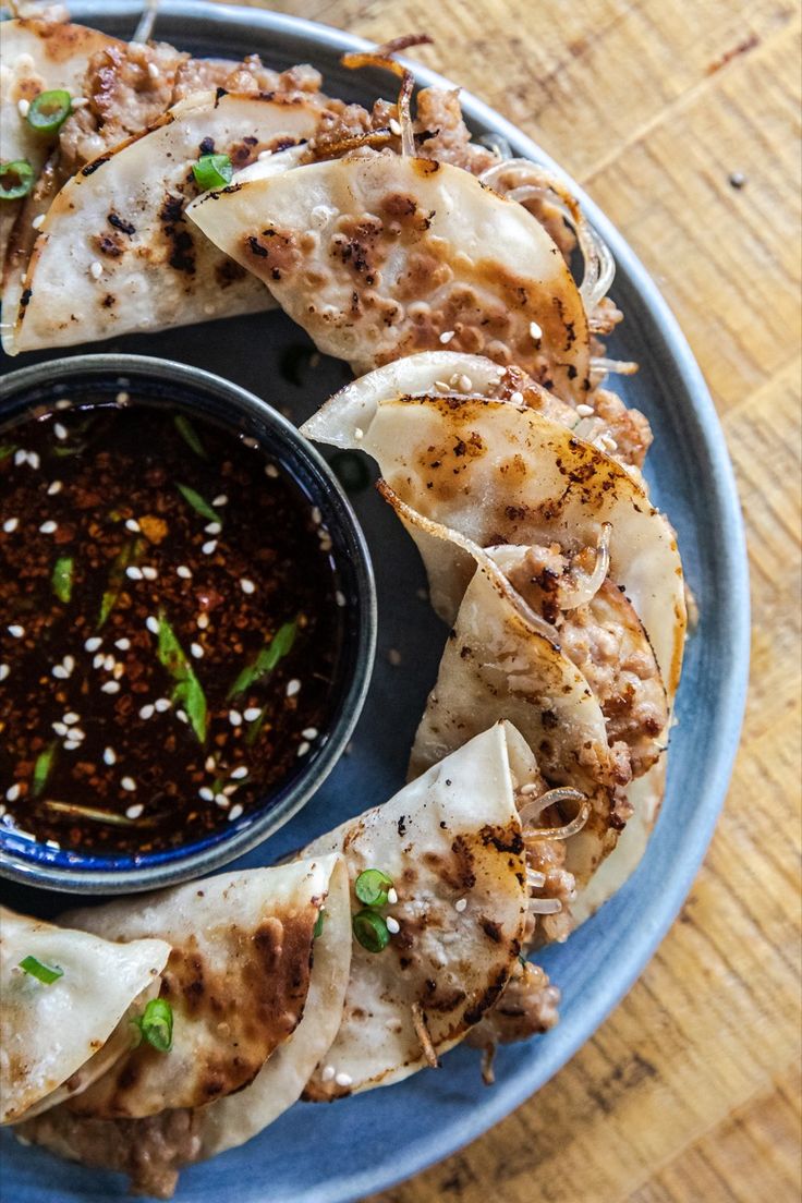 a blue plate topped with food on top of a wooden table next to a bowl of dipping sauce