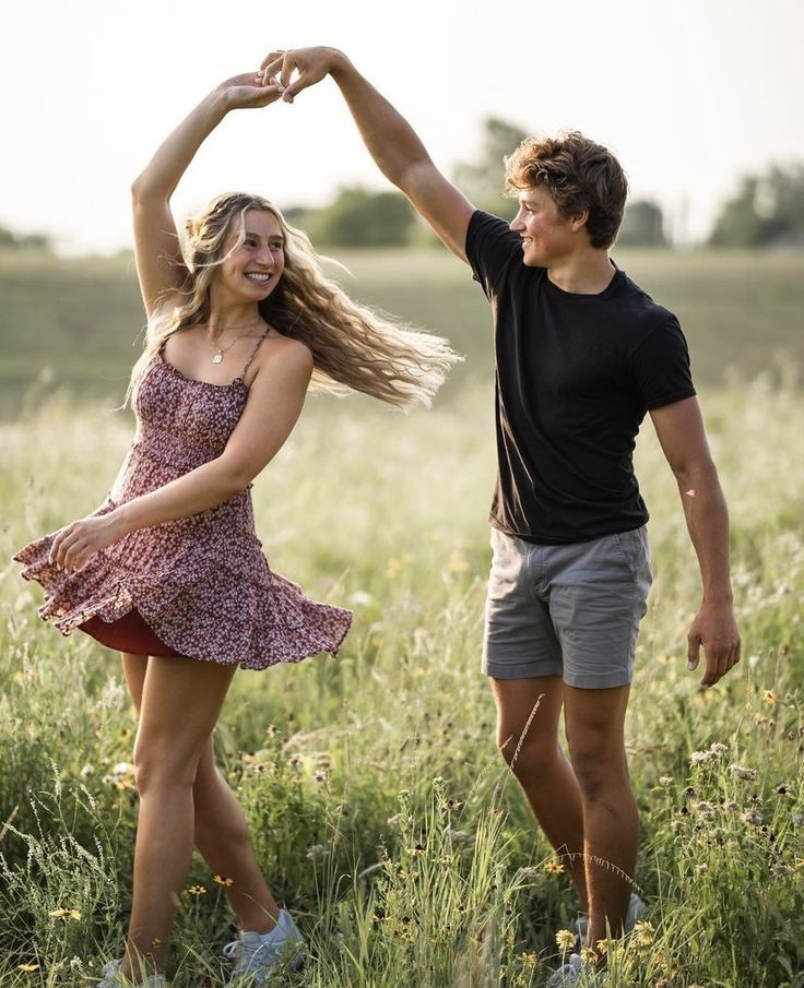 a young man and woman dancing in a field with their arms up to each other