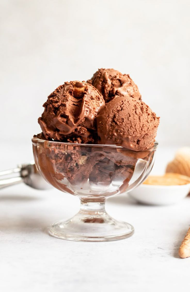 two scoops of chocolate ice cream in a glass bowl on a white counter top