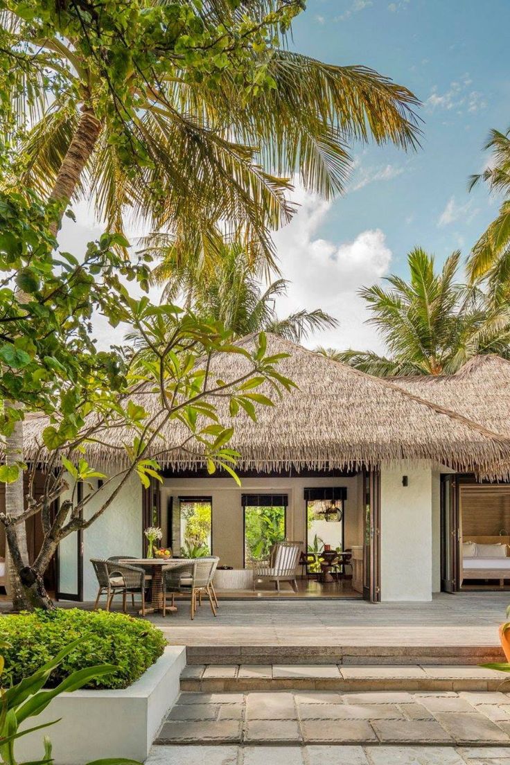 a house with a thatched roof and steps leading to the patio area, surrounded by palm trees