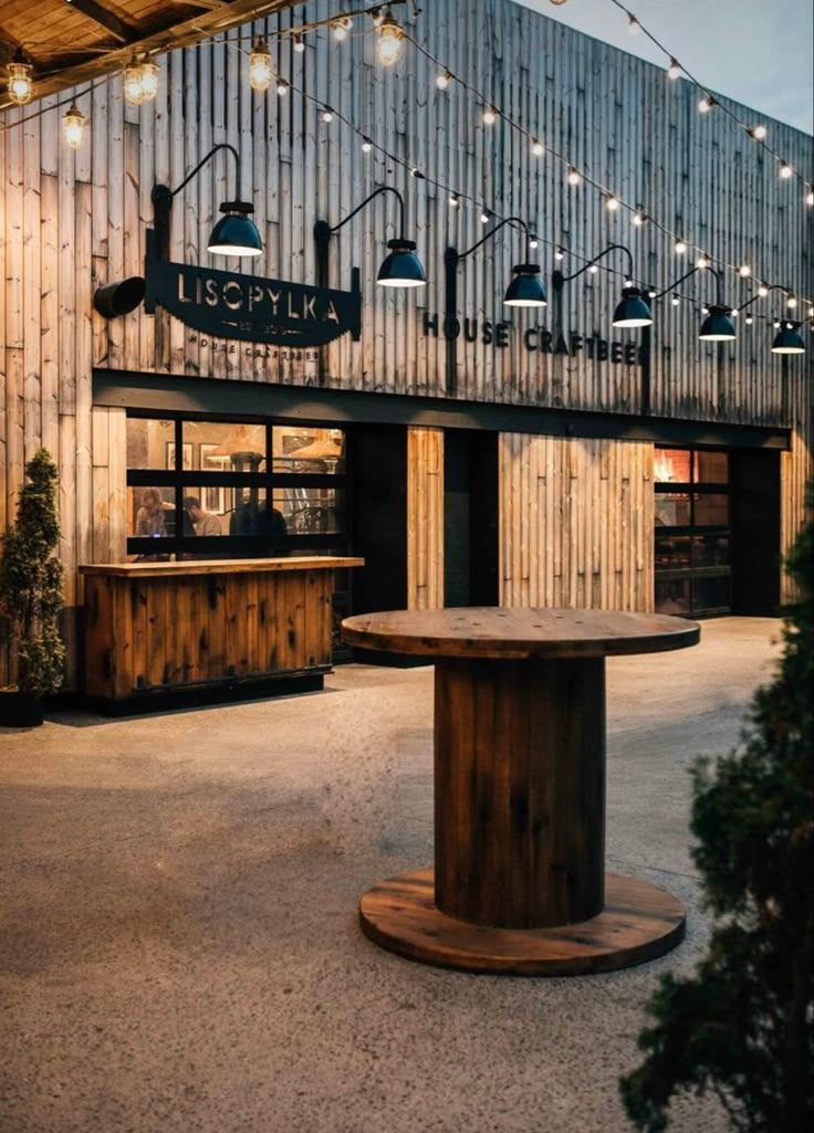 the outside of a restaurant with wooden tables and lights