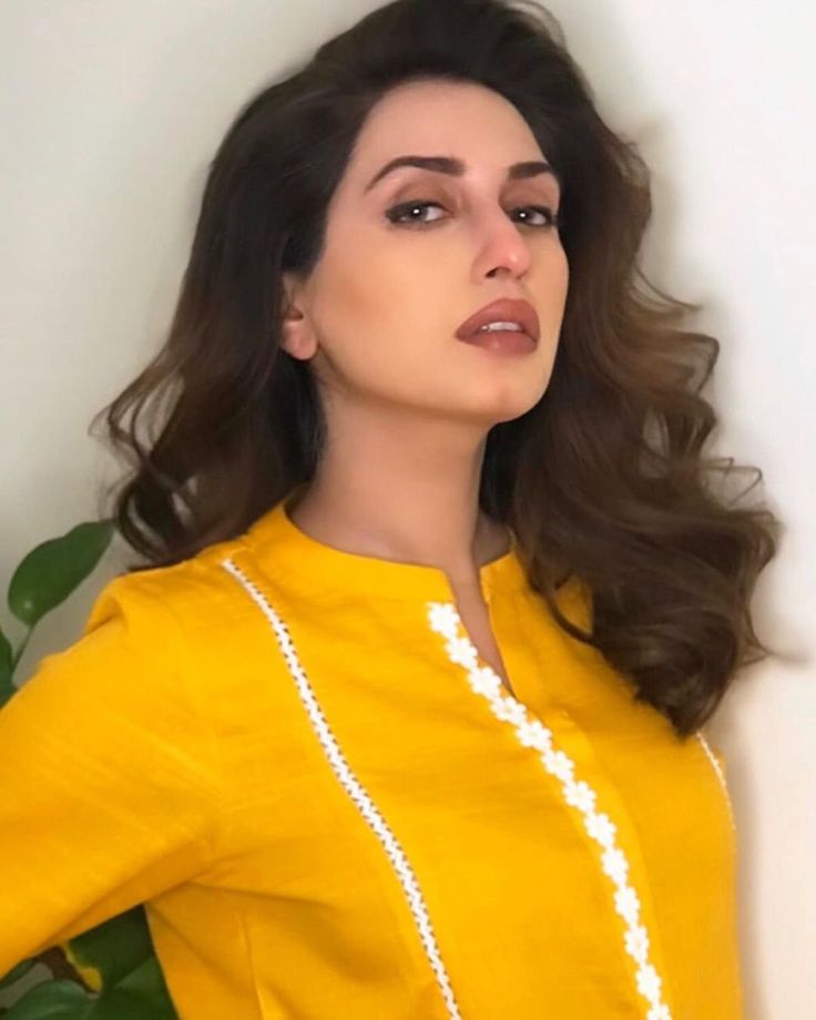 a woman with long hair wearing a yellow shirt and pearls on her necklace is posing for the camera