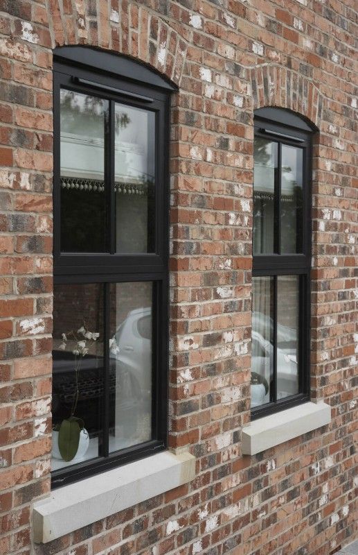 two windows on the side of a brick building with black panes and white trim