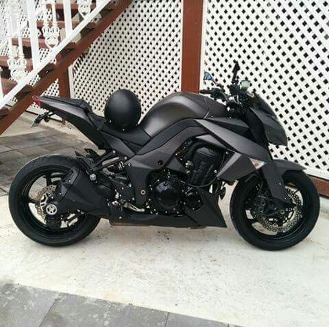 a black motorcycle parked on the sidewalk next to a white fence and wooden hand rail