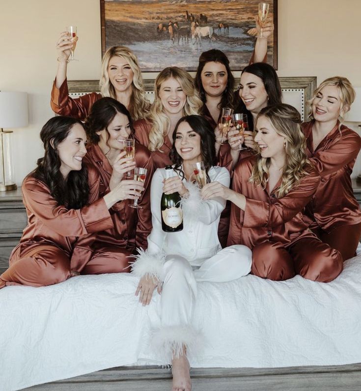 a group of women sitting on top of a bed holding wine bottles and posing for the camera