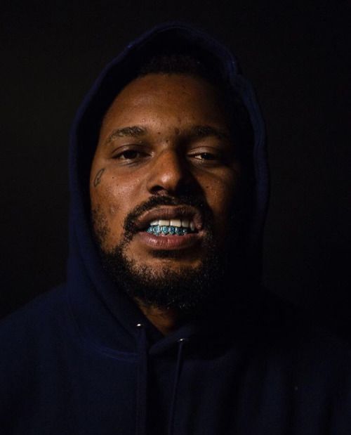 a man with a toothbrush in his mouth is looking at the camera while wearing a hoodie