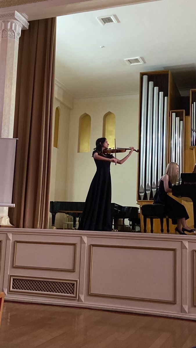 a woman is playing the violin in front of an organ while another person sits at a piano behind her