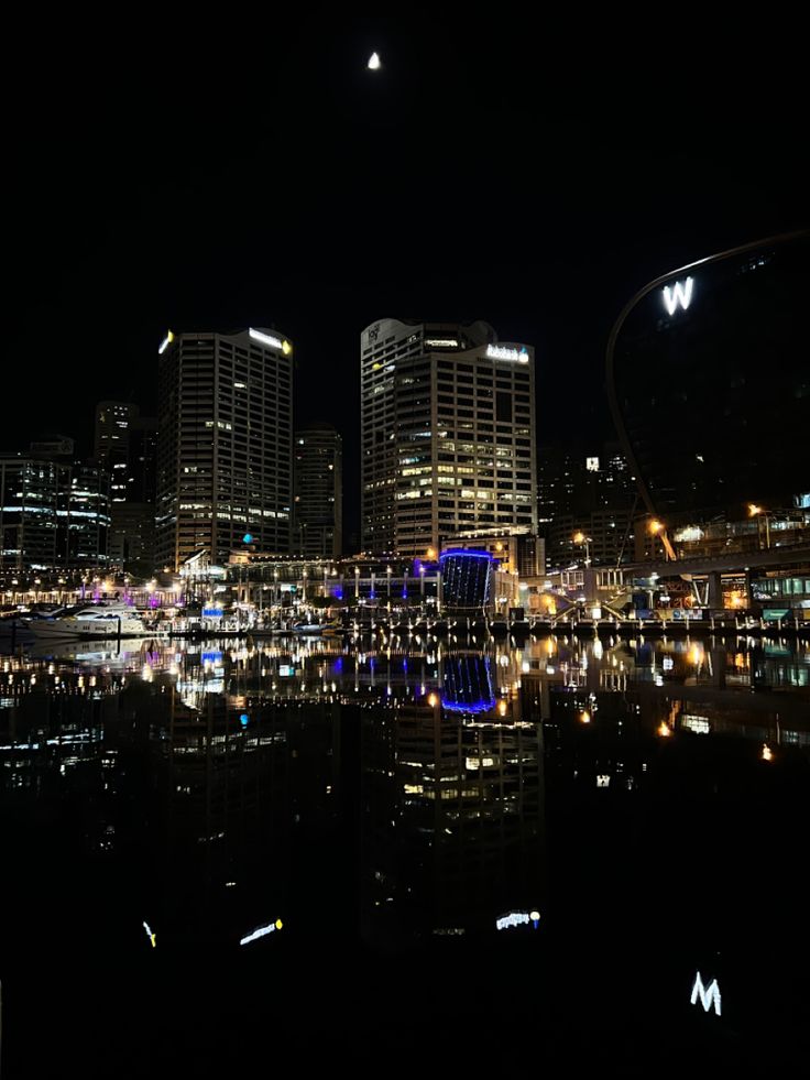 the city is lit up at night with lights reflecting in the water and skyscrapers