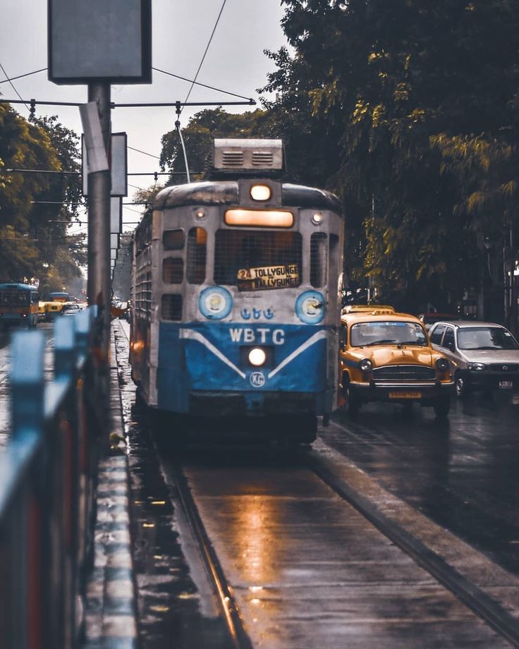 a blue and white train traveling down tracks next to a street filled with traffic on a rainy day