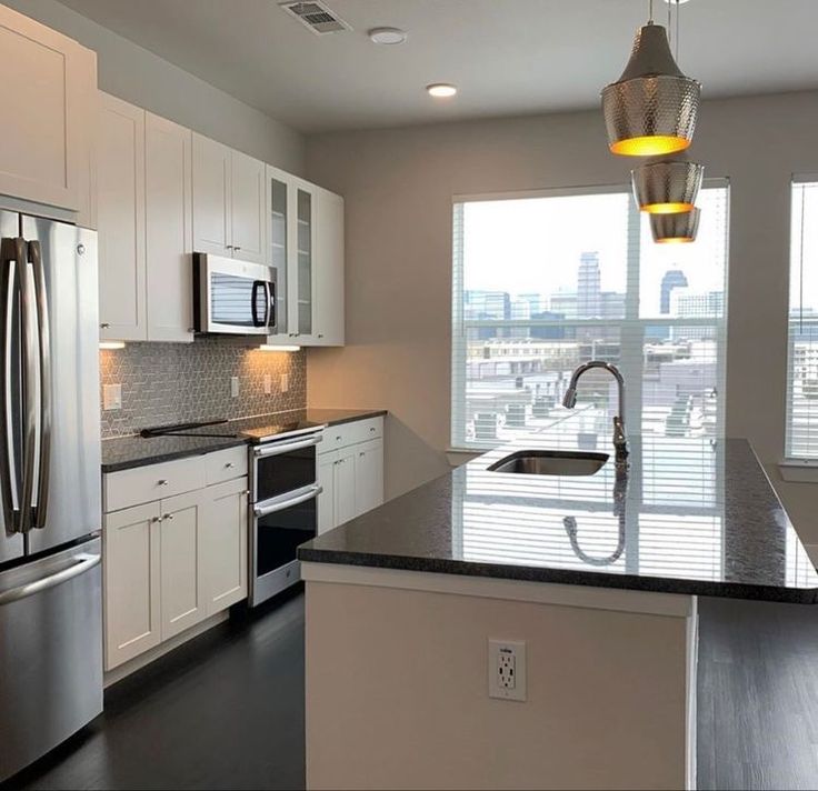 an empty kitchen with stainless steel appliances and white cabinetry, along with a large window overlooking the city