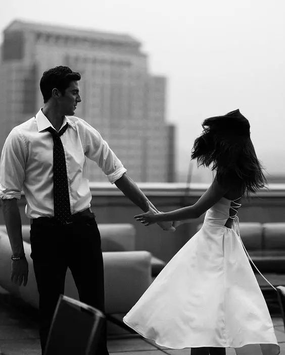 a man standing next to a woman on top of a roof with buildings in the background