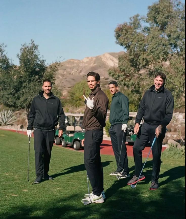 four men are standing on the grass with golf clubs in hand and one is pointing at something