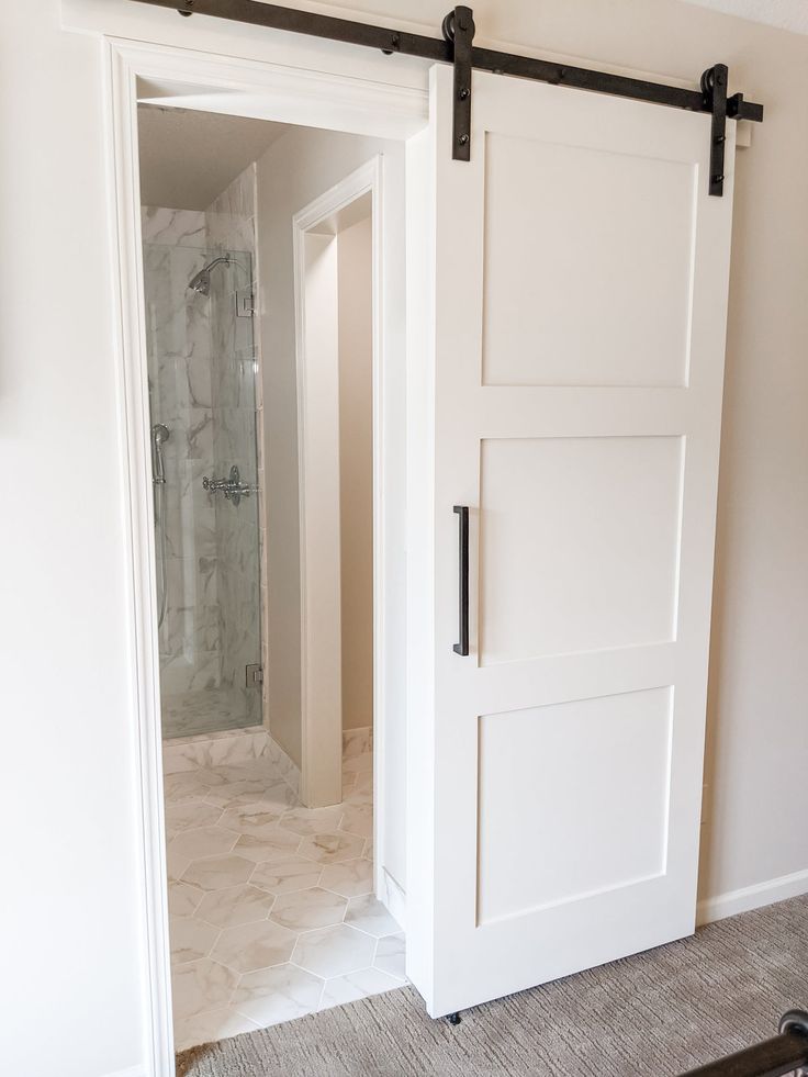 an open barn door in a bathroom with white walls and carpeted flooring on the floor