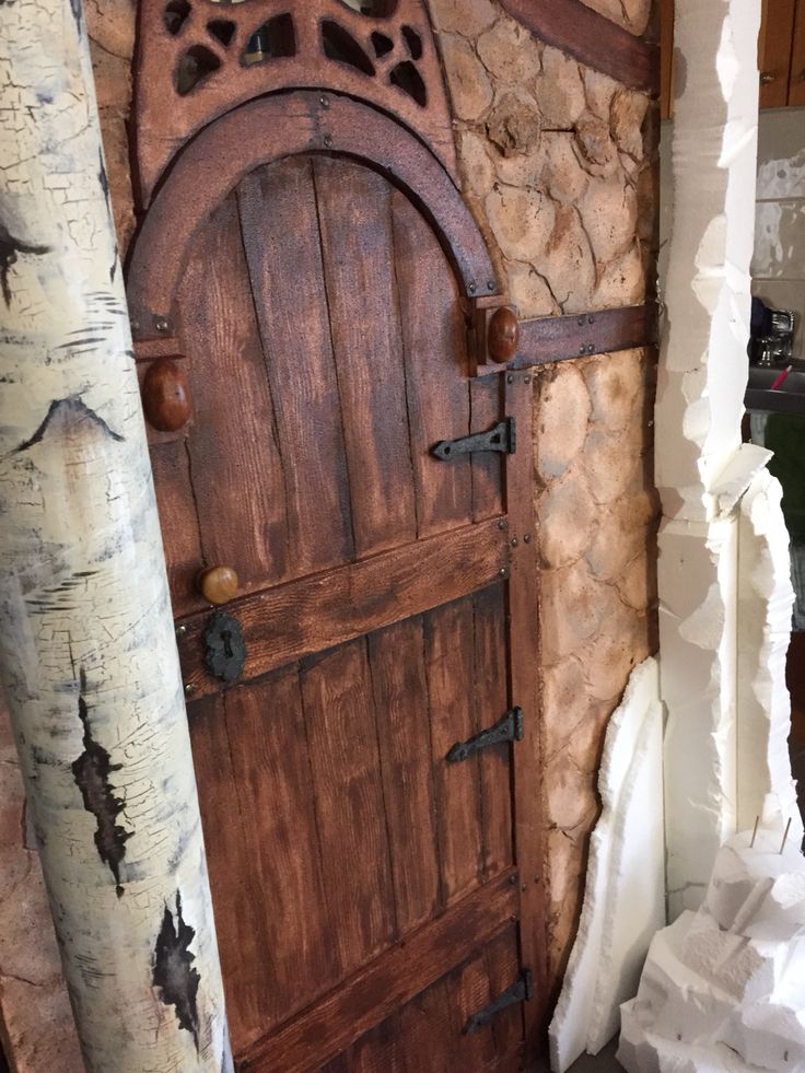 an old wooden door in the corner of a stone wall next to two birch trees