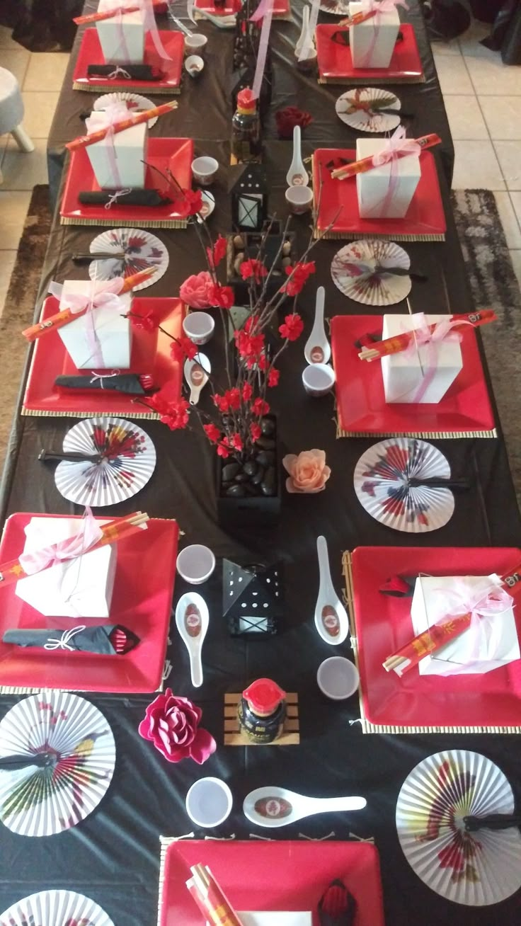 the table is set with red and white plates, napkins, silverware, and flowers