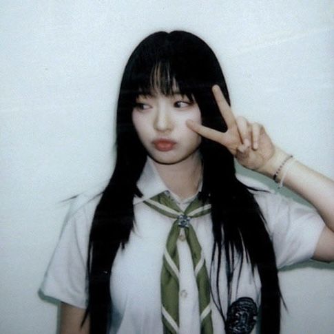 a girl with long black hair wearing a tie and making the peace sign while standing in front of a white wall