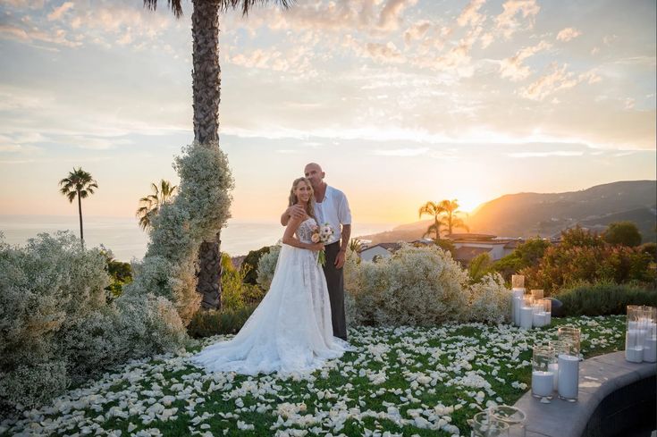 a bride and groom standing in front of the sunset at their wedding venue with flowers all around them