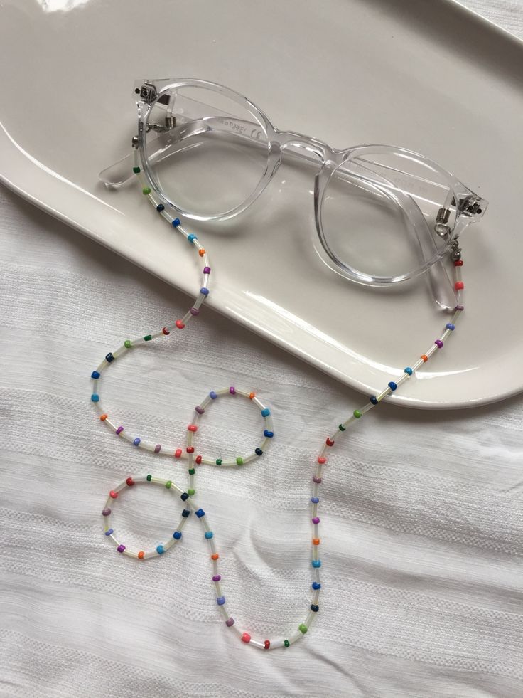 a pair of glasses sitting on top of a white plate next to a beaded necklace