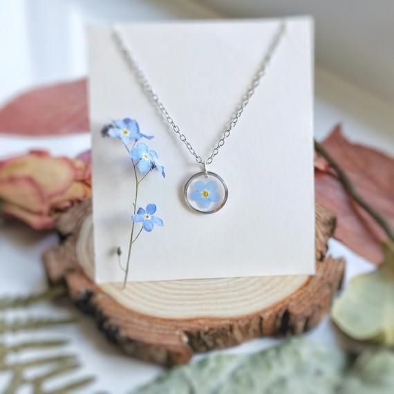 a necklace with blue flowers on it sitting next to a piece of paper and some leaves