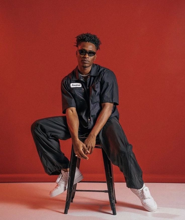 a man sitting on top of a stool wearing black pants and white sneakers with his legs crossed